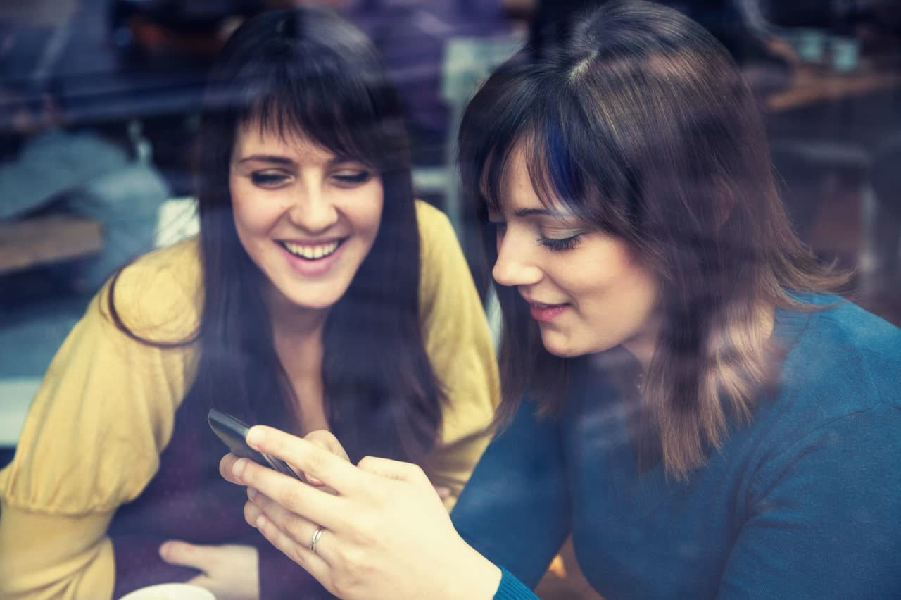 two women sit together and look at a smartphone screen